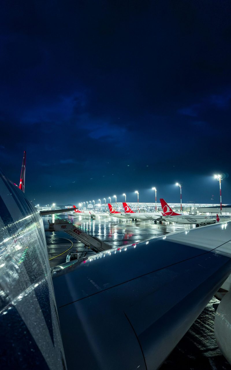 Illuminated airport with airplanes at night, view from aircraft wing.
